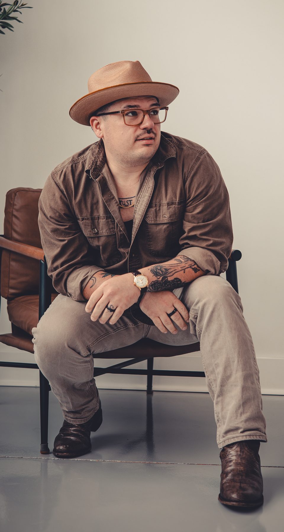 Keegan Sullivan in a hat and glasses, sitting forward in a leather chair